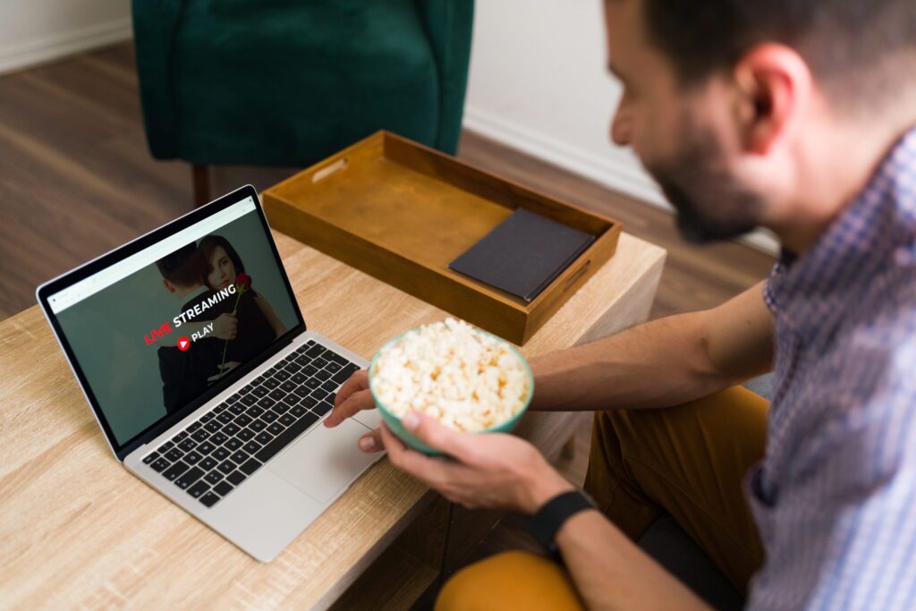 Man watching Hurawatch movies online free on laptop with popcorn