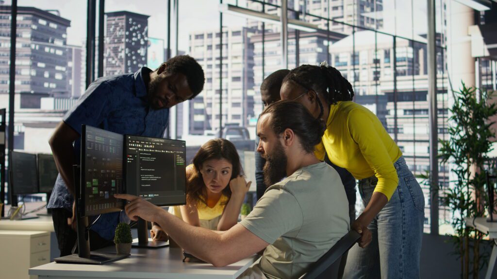 Software Engineering Explained: Process, Roles, and Best Practices (2026) A diverse software engineering team reviewing and discussing code on a monitor during a brainstorming session in a modern office