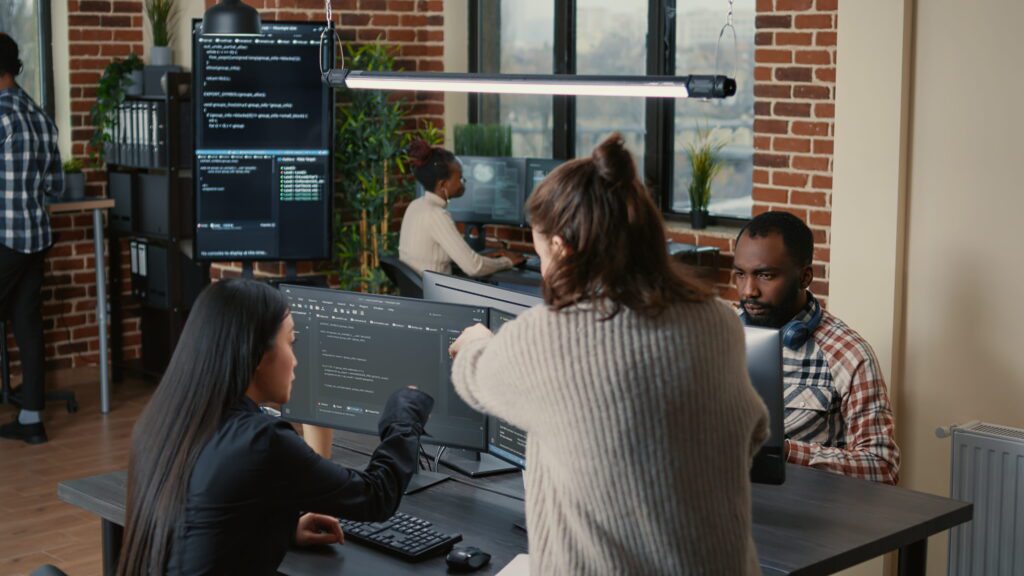 A diverse software engineering team reviewing and discussing code on a monitor during a brainstorming session in a modern office